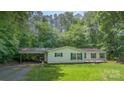 A charming home with green shutters and a covered parking area sits on a well-maintained lawn surrounded by mature trees at 611 W Robinson St, Dallas, NC 28034