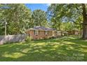 Quaint brick home with a lush lawn, shaded by mature trees, adjacent to a wooden privacy fence at 2522 Doster Rd, Monroe, NC 28112