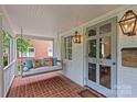 Charming front porch featuring a cozy porch swing, brick floor, and decorative lighting at 2814 Glendale Rd, Charlotte, NC 28209