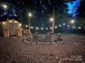 Outdoor fire pit with string lights and adirondack chairs surrounded by wooded area and shed at 8217 Lansford Rd, Charlotte, NC 28277