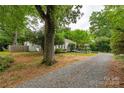 Exterior view of the house nestled amidst mature trees, showcasing the expansive gravel driveway at 34 Admiral Sw Ave, Concord, NC 28027