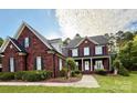 Charming two-story brick home featuring black shutters, a welcoming front porch, manicured landscaping, and a lush green lawn at 4230 Berry Hill Ct, Concord, NC 28025