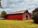 Classic red barn on a lush green field under a cloudy sky, surrounded by trees at 6714 Old Shelby Rd, Vale, NC 28168