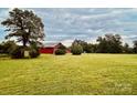 Large green field featuring a red barn and mature trees under a dramatic, cloudy sky at 6714 Old Shelby Rd, Vale, NC 28168