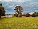Expansive green field featuring a red barn and a white storage shed in a rural setting at 6714 Old Shelby Rd, Vale, NC 28168