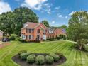 Expansive lawn with manicured landscaping surrounds this traditional brick home with mature trees and blue skies at 15737 Agincourt Dr, Huntersville, NC 28078
