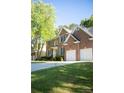An eye-level view of a traditional brick home featuring a two-car garage, green lawn, and mature shade trees at 7708 Harrington Woods Rd, Charlotte, NC 28269