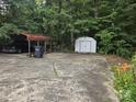Spacious concrete parking area with a metal carport, shed, mature trees, and flower garden at 9225 Robinson Church Rd, Charlotte, NC 28215