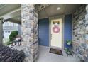Inviting front porch with a stone column, rocking chair, flower decor and a cheerful wreath on the pale-yellow door at 998 Emory Ln, Fort Mill, SC 29708
