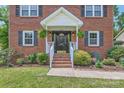 Close-up of front entrance with brick steps, white railings, and a black front door, accented by lush landscaping at 6221 Round Hill Rd, Charlotte, NC 28211