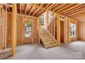 Unfinished interior featuring a wooden staircase and front door framed by exposed studs and beams at 4918 Buckingham Dr, Charlotte, NC 28209