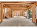 Unfinished living space with exposed studs, beams, staircase, and sliding glass doors to a patio at 4918 Buckingham Dr, Charlotte, NC 28209