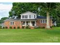 Charming two-story brick home features a covered front porch, manicured lawn, and mature trees at 7448 Forney Hill Rd, Denver, NC 28037