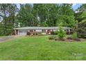 Single-story home with attached garage and well-manicured lawn, surrounded by lush trees in a peaceful setting at 2666 Providence Dr, Gastonia, NC 28052