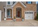 Inviting front entrance featuring brick steps, a stone archway, a stylish wood door, and a two-car garage at 12214 Bonny Oaks Dr, Cornelius, NC 28031