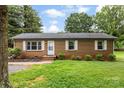 Inviting brick ranch home with landscaped front yard and mature trees under a sunny, blue sky at 1606 Northwoods Dr, Kings Mountain, NC 28086