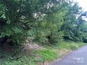 View of the heavily treed land available at this property. Paved street and dirt path visible at 7949 Ritter Dr, Charlotte, NC 28270