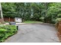 Expansive paved backyard with a basketball court, storage shed, and lush green surroundings at 3624 Moultrie St, Charlotte, NC 28209