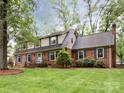 A view of a charming two-story brick home with manicured lawn on a lush, tree-lined lot at 6941 Queensberry Dr, Charlotte, NC 28226