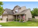 Inviting two-story home with a covered front porch, American flag, and a fenced yard at 225 Tasman Dr, Mount Holly, NC 28120