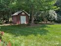 A backyard featuring a small storage shed, surrounded by green grass and flowering trees at 102 Rosewood Ln, Locust, NC 28097
