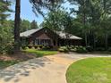 Single-story brick home featuring a curved driveway, mature trees, and manicured landscaping at 102 Rosewood Ln, Locust, NC 28097