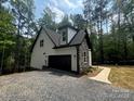 View of the home's exterior showcasing its architectural details, black garage door, stone, and gravel driveway at 248 Pioneer Dr, Mount Gilead, NC 27306