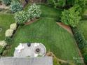 Aerial view of a meticulously landscaped backyard featuring a stone patio with a fire pit and lush greenery at 11324 Fullerton Place Nw Dr, Huntersville, NC 28078