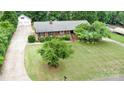Aerial view showcasing a brick ranch home, long driveway, detached garage, and mature landscaping at 115 Turner St, Lincolnton, NC 28092