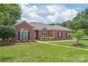 A view of a classic brick home with lush green lawn, blooming bushes, and manicured landscaping under a bright sky at 502 Roxanne Nw Ct, Concord, NC 28027