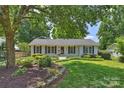 Charming white brick home featuring black shutters, a lush front lawn, and mature trees at 6938 Wrentree Dr, Charlotte, NC 28210