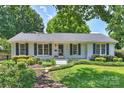 Charming white brick home featuring black shutters, a lush front lawn, and mature trees at 6938 Wrentree Dr, Charlotte, NC 28210
