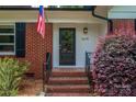 Close-up of front door with red brick, American flag, black door, and manicured shrubs at 1619 Flynnwood Dr, Charlotte, NC 28205