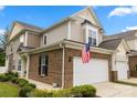Exterior view of a brick townhome with a two-car garage, American flag, and manicured landscaping at 44409 Oriole Dr # 200, Indian Land, SC 29707