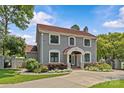 Beautiful two-story home with gray siding and a red tile roof with mature trees, professional landscaping and a gated driveway at 1619 Providence Rd, Charlotte, NC 28207