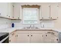 Close-up of the kitchen sink area featuring white cabinets, subway tile backsplash, and a window above the sink at 3043 Charles Rd, Shelby, NC 28152