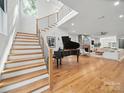 Bright entryway featuring hardwood floors, a grand staircase, a piano, and a view into the open living room with a fireplace at 708 Cross Trail Dr, Charlotte, NC 28204