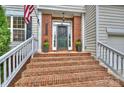 Inviting brick front porch with stairs, decorative plants, and a classic black front door at 14203 Queens Carriage Pl, Charlotte, NC 28278