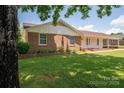 View of the charming brick home featuring a well-manicured lawn and lush, mature trees at 1613 Spangler Dr, Shelby, NC 28150