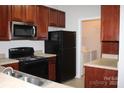 Efficient kitchen with wood cabinets, black appliances, and a laundry closet at 9823 Hyde Glen Ct, Charlotte, NC 28262