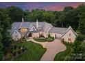 A stunning aerial view of an estate home with lush green lawn, mature trees, and warm exterior lighting at twilight at 8500 Longview Club Dr, Waxhaw, NC 28173