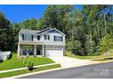 Two-story home featuring stone accents, light gray siding, black shutters, and a two-car garage with lush greenery background at 3816 Rosewood Dr, Mount Holly, NC 28120