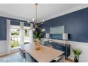 Stylish dining room featuring modern chandelier, blue accent wall with white crown molding, and a large picture window at 7800 Conifer Cir, Indian Trail, NC 28079