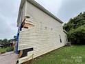 Side view of the damaged two-story home, with siding missing and a blue tarp covering exposed areas at 2012 Ashley Rd, Charlotte, NC 28208