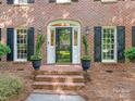 A close-up view of the red brick front entrance with black shutters and potted plants on the porch at 9622 Penshurst Trce, Charlotte, NC 28210