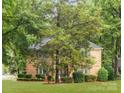 View of a brick two-story home with mature trees, a large lawn, and manicured landscaping at 4808 Cobble Glen Way, Charlotte, NC 28269