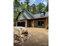 New construction featuring stone and green siding, a black garage door, and a charming front porch at 1923 Fairfield Rd, Mount Gilead, NC 27306