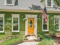 Close-up of the green home's entryway with an orange door, American flag, and potted plants, creating a welcoming entrance at 7639 Winterset Dr, Charlotte, NC 28270
