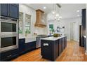 Modern kitchen featuring navy cabinets, a large island, stainless appliances, and a custom range hood at 7903 Tottenham Ct, Waxhaw, NC 28173