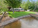 View of the backyard with lush lawn, mature trees, and dock leading to the water at 173 Riverwood Rd, Mooresville, NC 28117